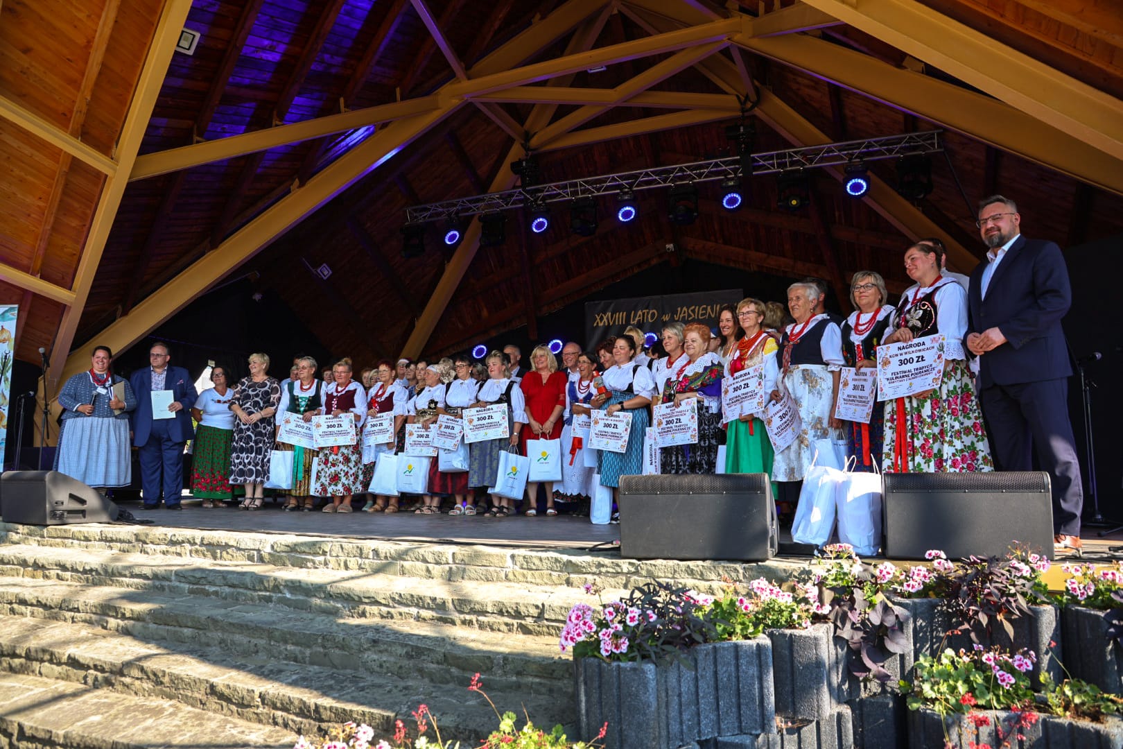 grupa ludzi stojąca na scenie w strojach ludowych